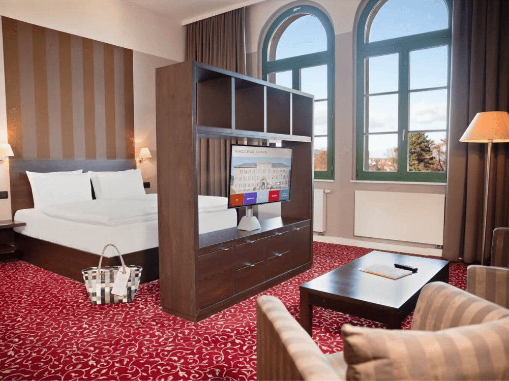 Junior Suite mit großem Doppelbett, Raumteiler mit TV, zwei Sesseln, Sofatisch, Wellnesstasche und großen Fenstern