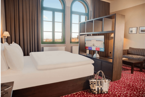 Zimmerblick Juniour-Suite mit Bett, TV Regal, Sofa, Wellnesstasche und großen Fenstern