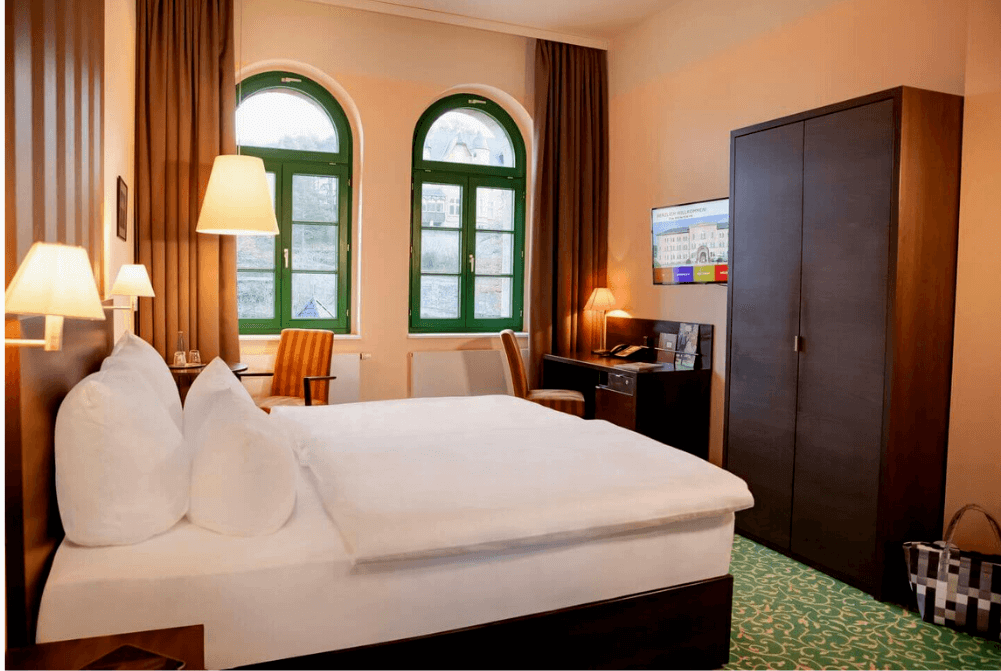 Junior Suite mit großem Doppelbett, Raumteiler mit TV, zwei Sesseln, Sofatisch, Wellnesstasche und großen Fenstern
