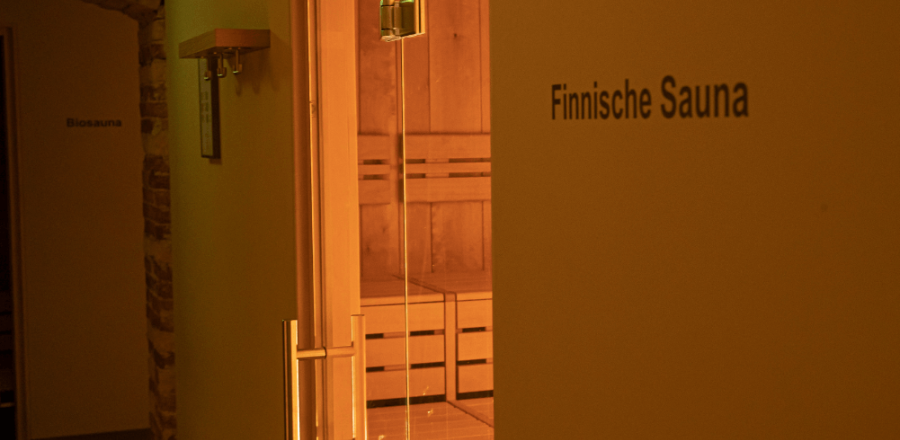 Blick in die Sauna durch eine Glastür mit Holzbänken und vorne Aufschrift Finnische Sauna