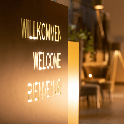 Willkommensschild am Empfang in der Hotellobby mit dem Wort Willkommen in Deutsch, Englisch und Französisch