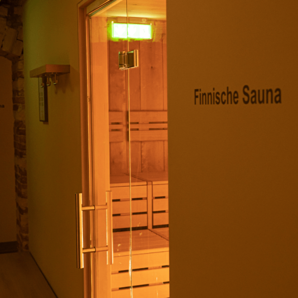 Blick in die Sauna durch eine Glastür mit Holzbänken und vorne Aufschrift Finnische Sauna
